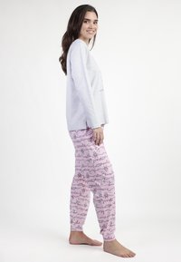 Camiseta de manga larga gris con estampado gráfico combinada con pantalones de pijama rosas que presentan un patrón repetido de dibujos y texto juguetón.