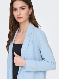 Light blue blazer with a tailored design, smooth texture, and long sleeves. Worn over a black top, featuring a notched collar.