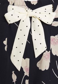 Tissu bleu marine à imprimé floral orné d'un grand nœud blanc à pois noirs à la taille, maintenu par une structure semblable à une ceinture.