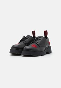 Chaussures en cuir noir avec détail brodé rouge, fermeture à lacets, semelle en caoutchouc et languette avec logo. Design épais pour une hauteur supplémentaire.