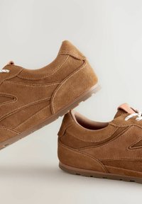 Braune Wildleder-Sneaker zeichnen sich durch ein niedriges Profil, weiße Schnürsenkel, ein strukturiertes Obermaterial und eine hellfarbige Gummisohle aus.