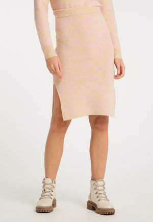Mannequin portant une jupe en maille beige longueur genou avec une fente latérale et un top assorti, associée à des bottines crème lacées avec des semelles épaisses.