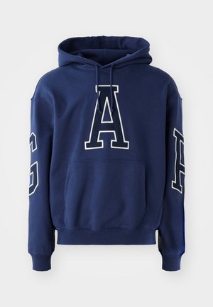 Marineblå hettegenser med kengurulomme, med hvite broderte bokstaver "G" og "A" på fronten og ermet, laget av et mykt stoff.