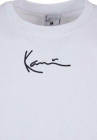 Biely sveter s čiernym vyšitou podpisovou grafikou na prednej strane. Klasický okrúhly výstrih a jemná textúra látky.