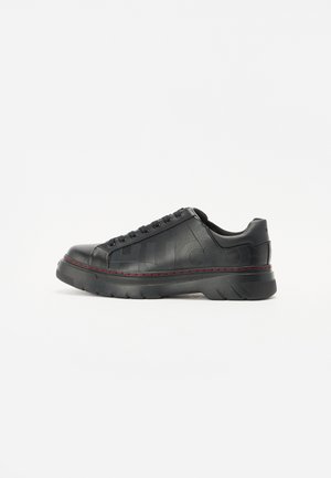 Czarny niski skórzany sneaker z wytłoczonym tekstem marki po boku i czerwonym przeszyciem wzdłuż grubej gumowej podeszwy, widoczny z profilu.