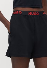 Svarta shorts med ett rött elastiskt midjeband märkt HUGO, med sidofickor och en avslappnad passform, tillverkade av mjukt och glatt textil.