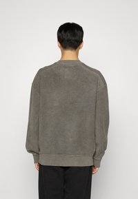 Sweat-shirt gris avec une finition douce et texturée, doté d'un col rond et d'une coupe décontractée, présenté sur un fond uni.