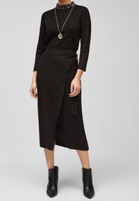 Czarny, długi rękaw, bluzka z wysokim kołnierzem ozdobiona ćwiekami, połączona z czarną spódnicą typu wrap związaną w talii. Botki na obcasie sięgające do kostek.