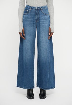 Platas kāju zils denim džinsus ar augstu jostasvietu, divām priekšējām kabatām un tīru šuvi. Materiāls izceļ klassisku denim tekstūru un krāsu.