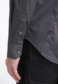 Grå knapp-up skjorta med en mjuk textur, med en spetsig krage, långa ärmar och detaljer med två knappar vid manschetten. Tyget verkar vara något glansigt.