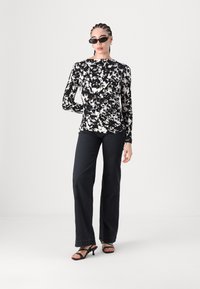 Langärmliges Oberteil mit schwarz-weißem Blumenmuster, kombiniert mit dunkelblauen weit geschnittenen Jeans und schwarzen Riemchen-Absätzen. Das Model trägt schwarze Sonnenbrillen.