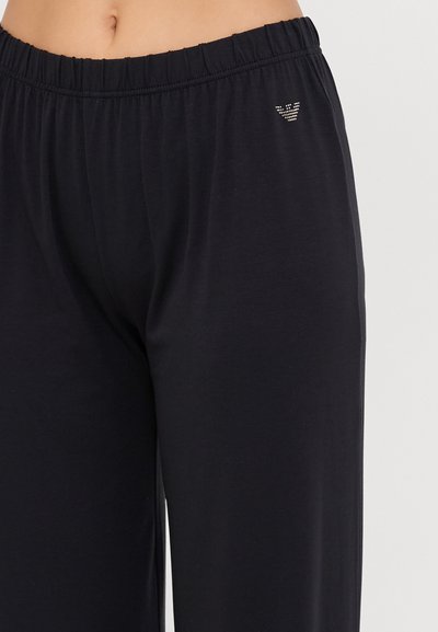 Pantaloni lounge neri realizzati in un tessuto morbido con vita elastica. Presentano un piccolo dettaglio di logo in strass sull'anche.