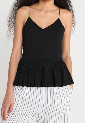 Haut sans manches noir avec un décolleté en V et un ourlet à volants. Fait en tissu doux, avec des bretelles spaghetti fines. Associé à un pantalon rayé blanc.