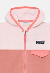 Flis jakna s kapuco v roza in koralnih odtenkih, z zadrgo in žepom na prsih, ki prikazuje logo Patagonia Kids.