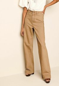 Leveälahkeiset khakinväriset housut, joissa on korkeavyötärö, valmistettu teksturoidusta puuvillasta. Housuissa on etutaskut ja tikkaukset saumoissa. Yhdistetty ruskeisiin korokepohjakenkiin.