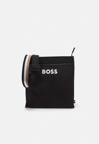 Sort nylon skuldertaske med en øverste lynlås, med en hvid logo og en stribet rem i sort, hvid og beige. Kompakt firkantet design.