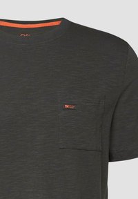 T-shirt gris foncé à manches courtes avec une poche poitrine ornée d'une petite étiquette orange « Elevated Casual » et un liseré orange à l'intérieur du col.