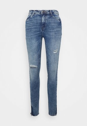 Jeans skinny em denim azul médio com um design desgastado, incluindo rasgos nos joelhos e zíperes nas bainhas para um ajuste ajustável.