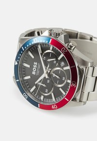 Montre chronographe en acier inoxydable avec un cadran noir, une lunette bleu et rouge, et trois sous-cadrans. Elle dispose d'index horaires lumineux et d'accents argentés.