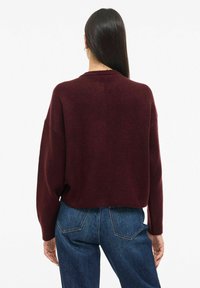 Burgunderroter Strickpullover mit lockerem Schnitt, überschnittenen Schultern und rundem Ausschnitt, kombiniert mit hoch taillierten blauen Jeans aus Denim. Strukturierter Stoff.