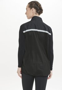 Svart idrottsjacka med en reflekterande horisontell rand över den övre ryggen, nätstruktur och en lös passform.