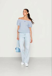 Top listrado de ombros à mostra em azul e branco, com mangas curtas bufantes, combinado com jeans azul claro e uma pequena bolsa azul. Ténis brancos.