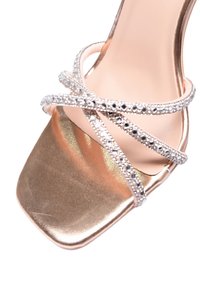 Sandalo alto in metallo dorato con punta quadrata. Presenta cinturini incrociati decorati con strass, aggiungendo brillantezza e dettagli.