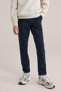 Tumši zili svārki, kas kombinēti ar krēmkrāsas džemperi; ar ribotu aproču un apkakles dizainu. Kājas apavi ir bēšas un pelēkas sporta kurpes ar sieta akcentiem.