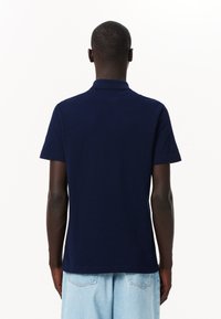 Meripaidasta, jossa on lyhyet hihat ja klassinen kaulus. Valmistettu sileästä puuvillakankaasta. Yksinkertainen malli ilman näkyviä kuvioita tai yksityiskohtia.