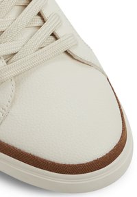 Zapatilla de cuero color crema con superficie texturizada, acentos de tela marrón y cordones beige. Presenta una punta redondeada y una suela de goma.