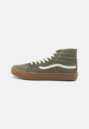 Høj olivegrøn sneaker med hvide snørebånd, hvid sideribbe og brun gummisål på en ensartet lys baggrund.