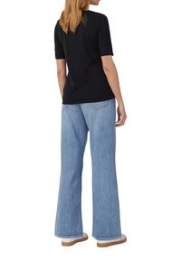 T-shirt noir à manches courtes associé à un jean large bleu clair. Le jean a une coupe décontractée et une couture contrastante. Des baskets blanches complètent le look.