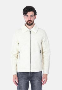 Giacca beige foderata in shearling con chiusura a zip, due tasche laterali con zip e un ampio colletto. Texture liscia con sottili dettagli di cucitura.