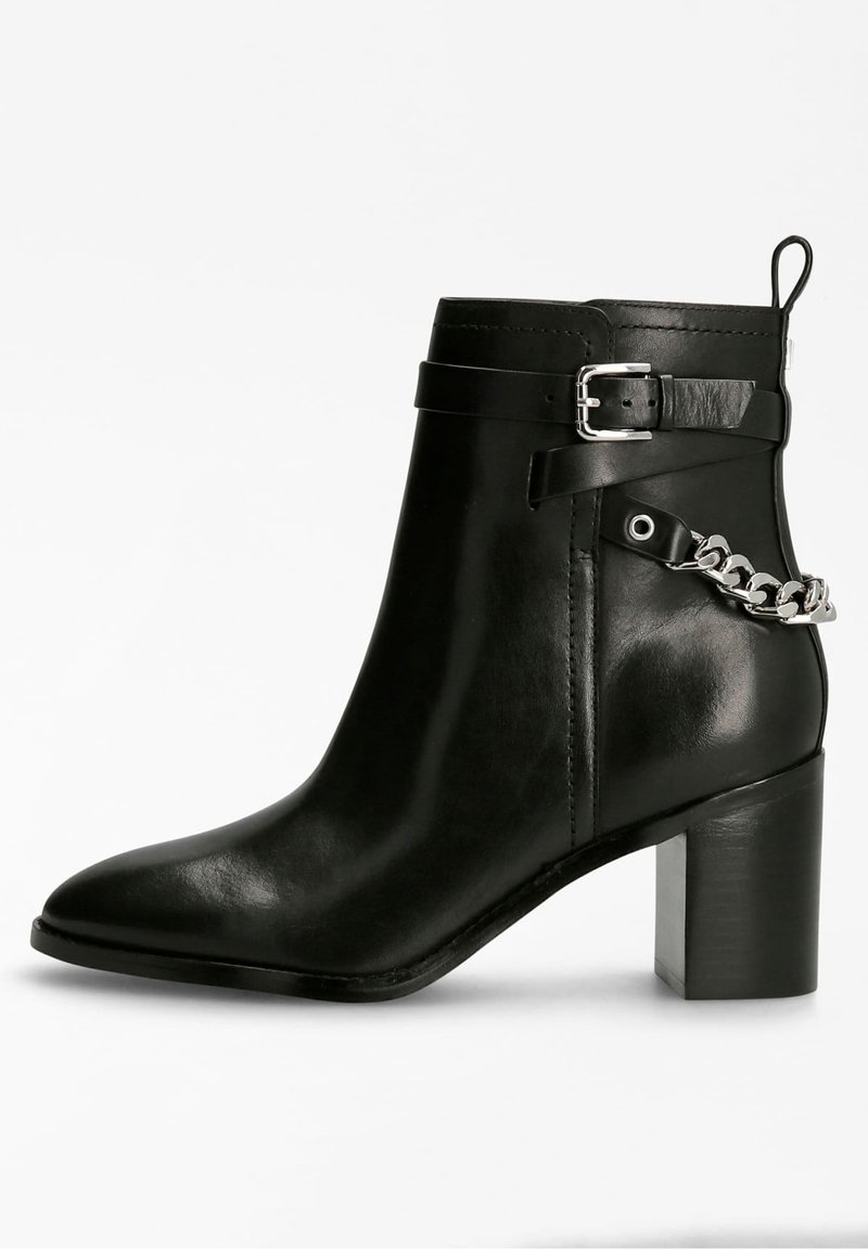 Bottine noire en cuir avec talon bloc, bout pointu, bride décorative avec boucle argentée et détail chaîne argentée autour de l'arrière.
