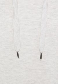 Gros plan sur un tissu blanc avec deux cordons de capuche blancs tressés se terminant par des embouts métalliques argentés.