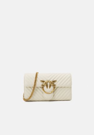 Sac en cuir matelassé couleur crème avec un accent en métal doré en forme de cercle représentant deux oiseaux. Comprend une bandoulière en chaîne dorée pour le porter.