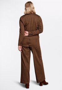 Brun mönstrad set som består av en långärmad topp och vida byxor. Tyget har en geometrisk design med en slät yta. Bruna klackar bärs.