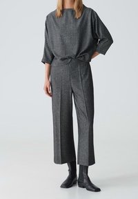 Top de punto texturizado gris con mangas anchas, combinado con pantalones grises de cintura alta y pliegues. La modelo lleva botas de tobillo ajustadas en negro.
