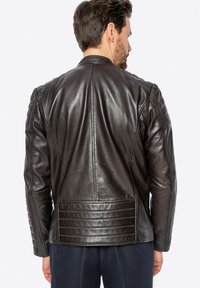 Giubbotto di pelle marrone caratterizzato da una texture liscia, design trapuntato sulle spalle e sulla schiena, con accenti di cucitura verticale e una vestibilità su misura.