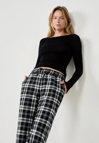 Blusa negra de manga larga con un diseño ajustado, combinada con pantalones de pijama sueltos de cuadros en blanco y negro, que cuentan con una cintura elástica y bolsillos.