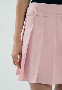 Różowa plisowana spódnica z usztywnionym pasem i szlufkami na pasek, wykonana z gładkiego materiału, z wyraźnymi, równymi fałdami i czystymi brzegami.