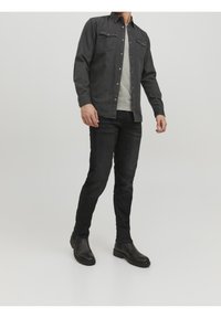 Czarna koszula dżinsowa z dwoma kieszeniami na piersi, szary t-shirt z okrągłym dekoltem pod spodem, czarne jeansy slim fit oraz czarne botki na kostkę. Gładka faktura.