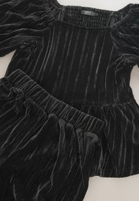 Czarny welwetowy zestaw składający się z dwóch części, z zebranym dekoltem i bufiastymi rękawami. Góra ma fason peplum, a talia jest elastyczna.