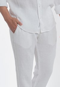 Witte linnen overhemd met een knoopsluiting aan de voorkant en opgerolde mouwen, gecombineerd met bijpassende witte linnen broeken met zijzakken en een relaxte pasvorm.
