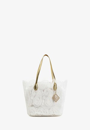 Hvid blonde-tote taske med gyldne håndtag og en gylden firkantet charme, der hænger fra et håndtag.