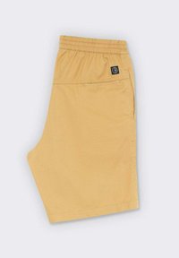 Pantalones cortos amarillos hechos de una tela suave. Cuentan con una cinturilla elástica, un parche con el logo y un bolsillo lateral. Diseño simple con líneas limpias.
