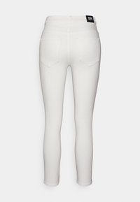 Jeans skinny de algodón blancos con una cintura alta, dos bolsillos traseros y una etiqueta de marca negra en la cinturilla. Textura suave y diseño ajustado.
