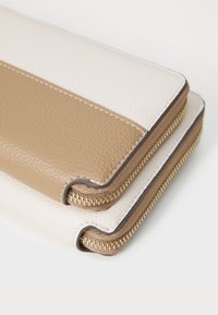Portefeuille texturé en beige et crème, doté d'une fermeture éclair et de coutures contrastées. Cuir synthétique lisse avec un design superposé.