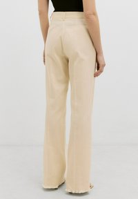 Beige wijde broek met een zachte textuur, voorzien van een hoge taille en rafelige zoomdetails, die een comfortabele pasvorm bieden voor casual dragen.