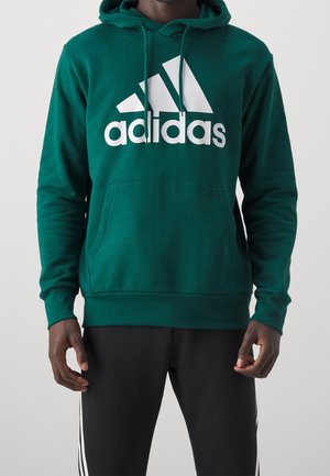 Sudadera verde hecha de tela suave, con un gran logo blanco de adidas, bolsillo tipo canguro, capucha ajustable con cordón y puños acanalados.